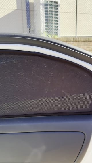 A custom-fit magnetic mesh sun shade fitted to a car window