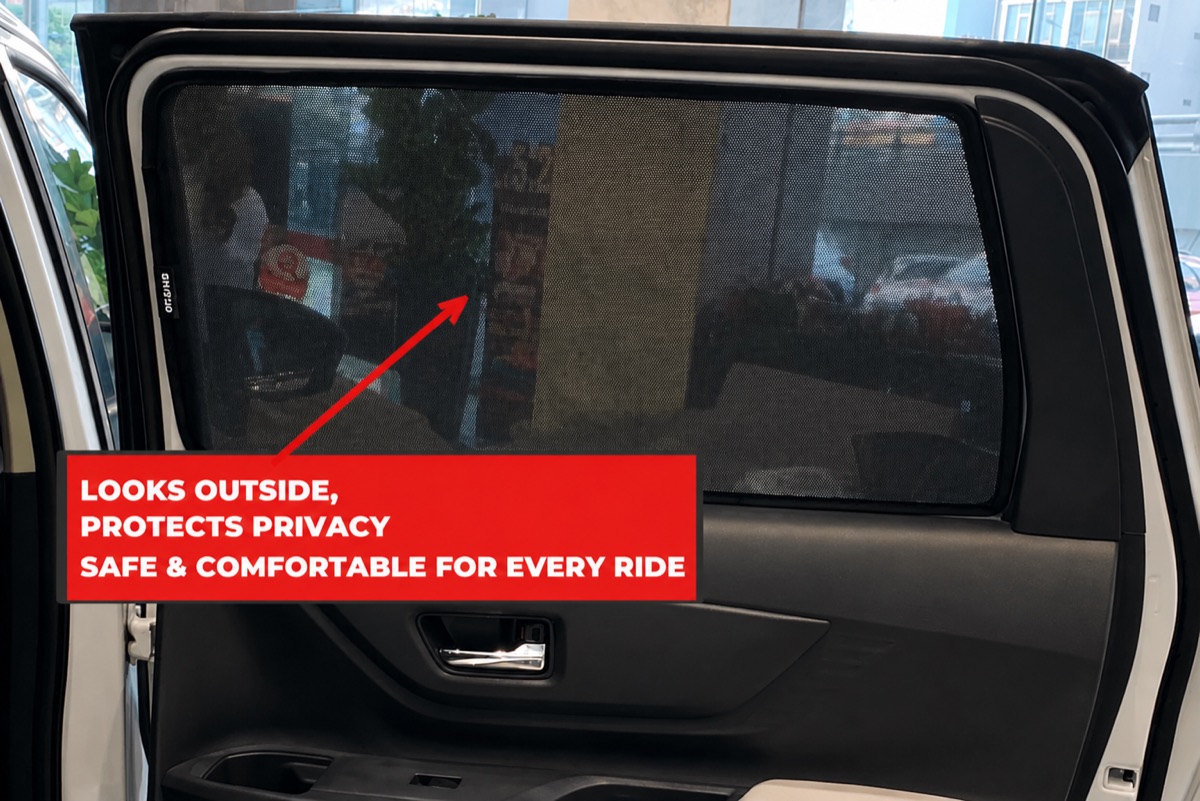 A fitted rear-door window shade seen from inside the car. The street, parked cars and shopfronts outside are clearly visible through the mesh.